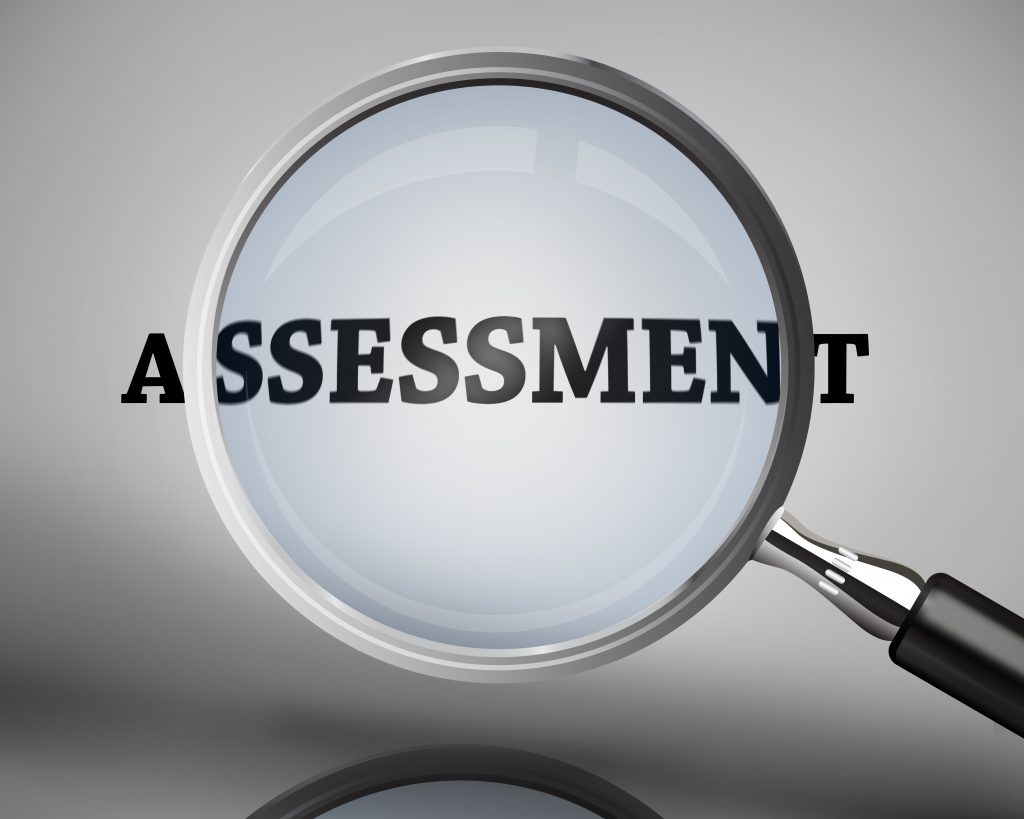 Magnifying glass showing assessment word on grey background